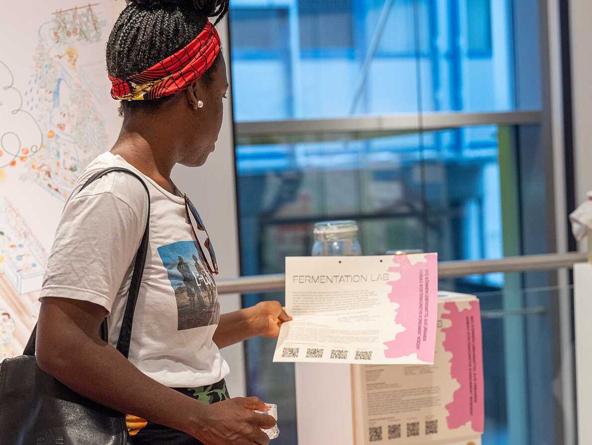 Eine Person betrachtet in der Ausstellung "Different Futures Make A Dialogua" einen Infozettel, welcher über das Szenario "Ernährung" informiert